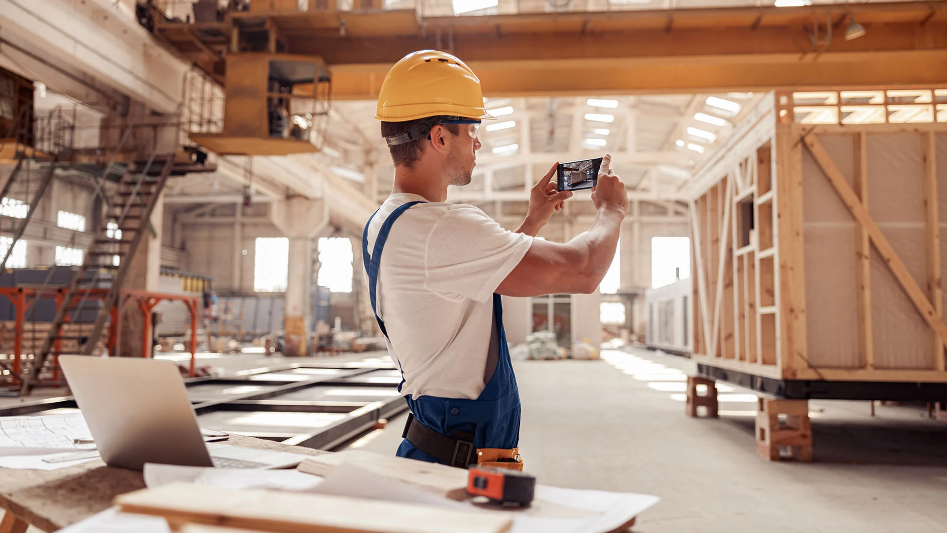 Construction worker in a safety helmet capturing site progress with a smartphone with homearize flooring software inside a modern factory warehouse.